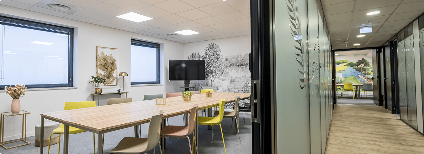 Salle de réunion du centre B’Coworker à Roubaix, avec grande table, chaises colorées, écran et cloisons vitrées, BMG Foncière.