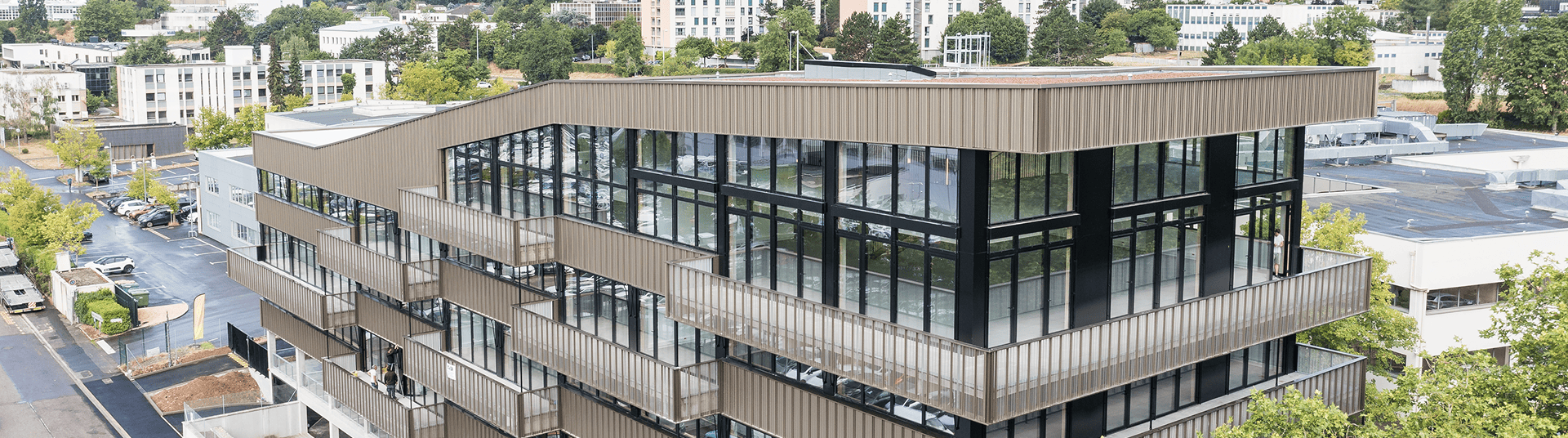 Vue en hauteur du bâtiment Le Phénix à Laxou, montrant l’angle vitré, les façades et les abords routiers, BMG Foncière.