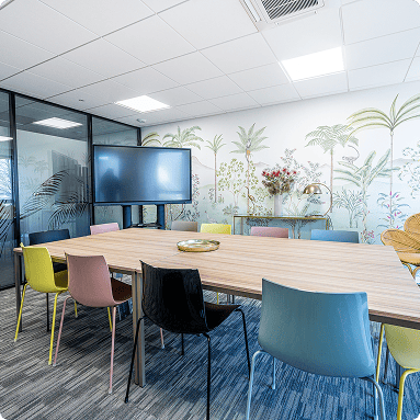 Salle de réunion avec grande table, chaises colorées et écran mural dans l’espace B’CoWorker à Villers-lès-Nancy.