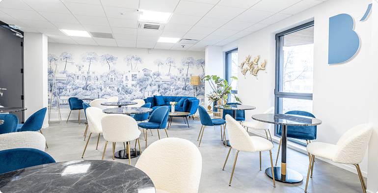 Espace convivial B’CoWorker à Villers-lès-Nancy avec fauteuils bleus, tables basses, fresque murale et logo visible sur le mur.